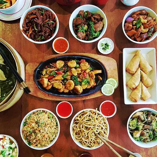 Mister Wok communal table spread — abundant shared dishes from the Two Rivers wok kitchen, community dining at its finest